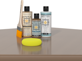 Retique It® Barn Wood kit with brush, Barn Wood stain alternative, gloss top coat, and yellow sponge on a wood surface.