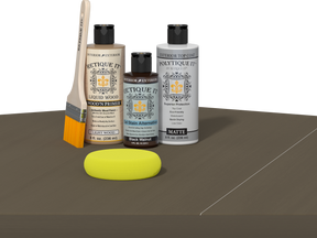 Retique It Black Walnut Kit with Matte Polytique It, Light Wood Wood'n Primer, Black Walnut Gel Stain Alternative, paintbrush, and yellow sponge on a tabletop.
