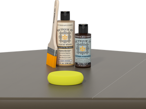 Retique It Black Walnut Kit with Light Wood Wood'n Primer, Black Walnut Gel Stain Alternative, paintbrush, and yellow sponge on a tabletop.