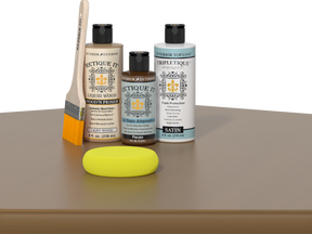Retique It® Light Wood kit with brush, Pecan stain alternative, satin top coat, and yellow sponge on a wood surface.