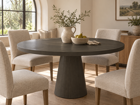 Round Carbon Gray pedestal dining table surrounded by cream upholstered chairs in a bright dining nook.