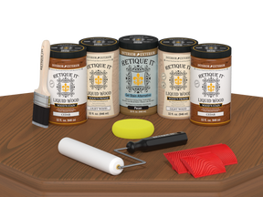 Retique It Cedar Wood'n Kit featuring Cedar Liquid Wood stain, Light Wood primer, Pecan Gel Stain Alternative, paint brush, white roller, yellow sponge, and red graining tools displayed on a wood tabletop.