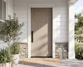 A modern single-panel wood front door with a vertical black handle, set in a white shiplap entryway with stone accents, a woven doormat, and potted plants.