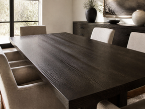 A dark wood dining table with a prominent grain, surrounded by beige upholstered dining chairs in a modern dining room setting.